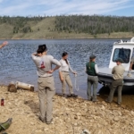 A group of people standing next to a boat on a lake.