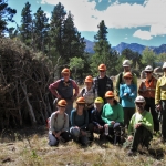 A group of people posing in front of a pile of wood.