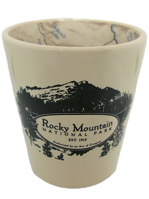 A shot glass featuring black illustrations of mountains and trees. Text reads: "Rocky Mountain National Park Map Est. 1915 Authorized by an Act of Congress.
