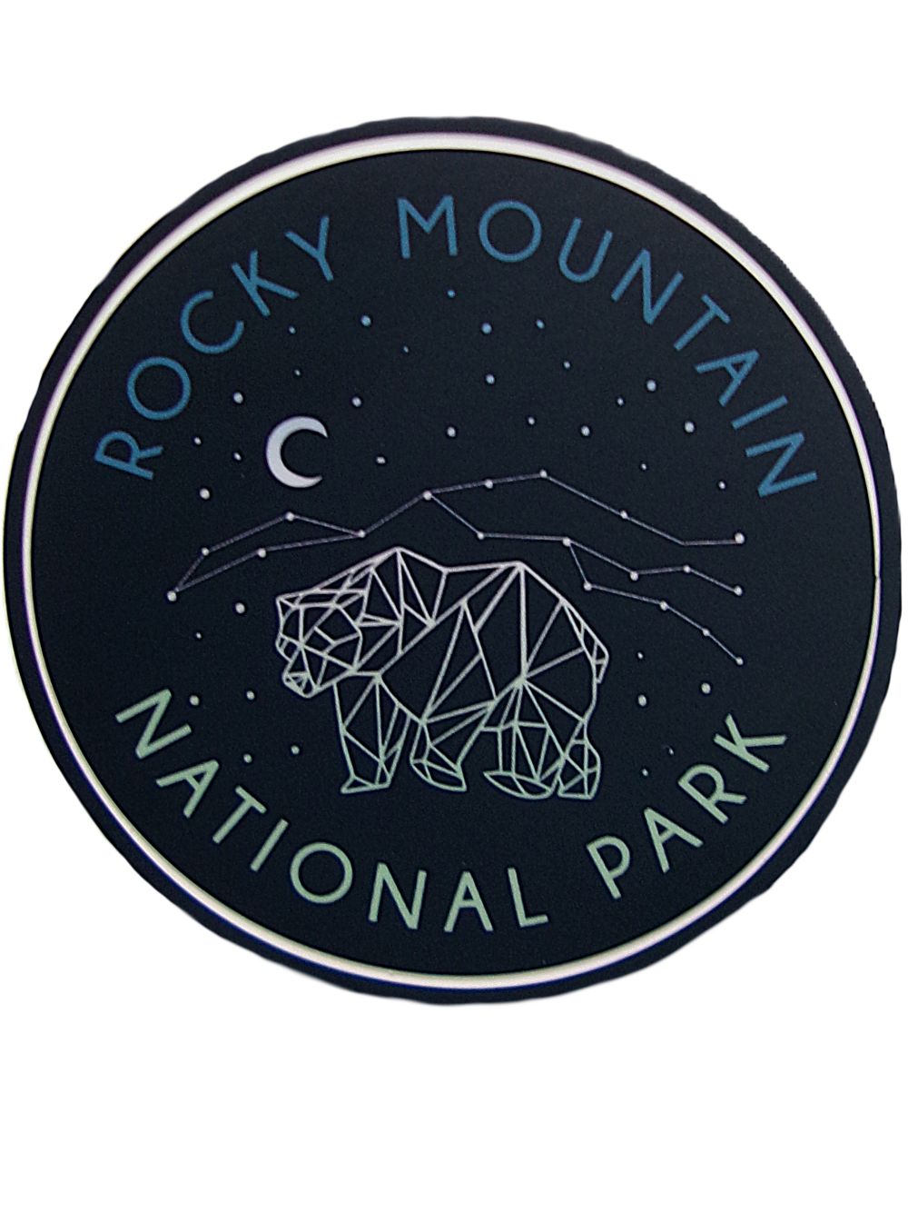 Circular "Sticker - RMNP Bear Constellation" featuring a geometric bear design beneath a starry sky with "Rocky Mountain National Park" text and crescent moon.