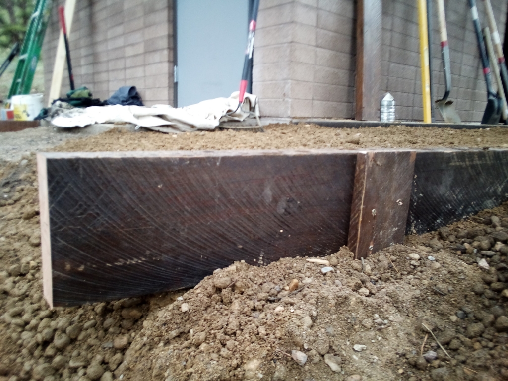 A piece of wood is sitting in the dirt next to a building.