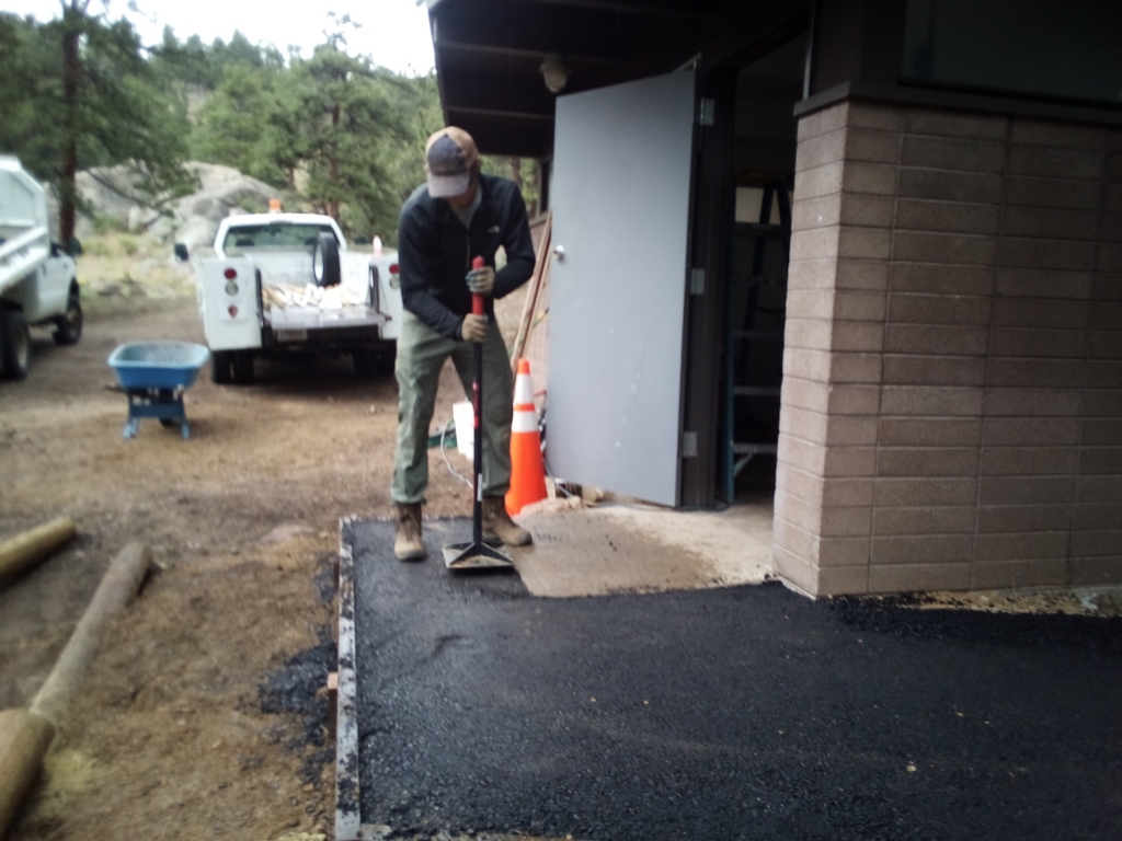 A man is laying asphalt on a sidewalk.