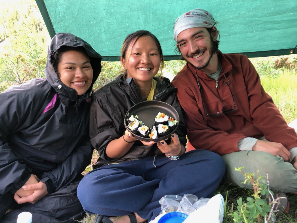 Three people sitting under a green tarp.