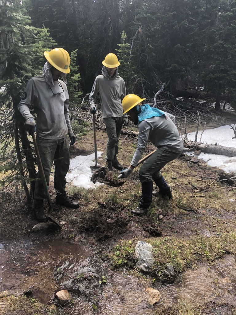 Three men in hard hats working in a muddy area.