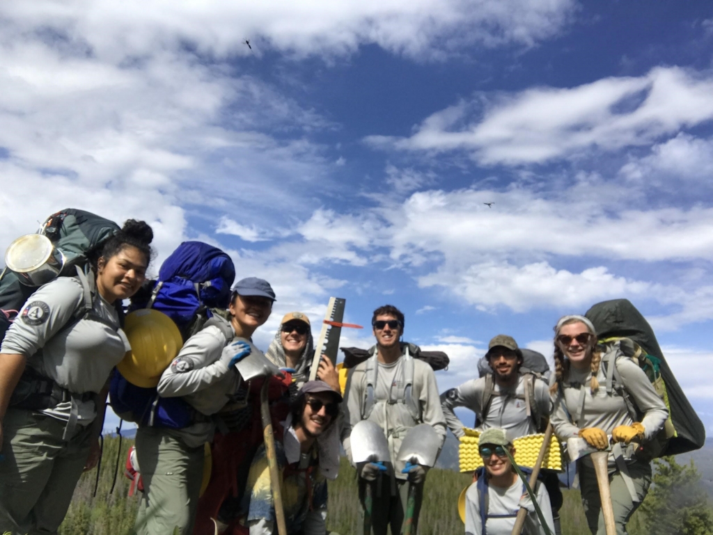 A group of people with backpacks and shovels posing for a photo.