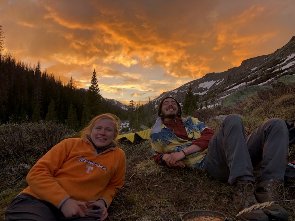 Two people sitting on the ground in front of a sunset.
