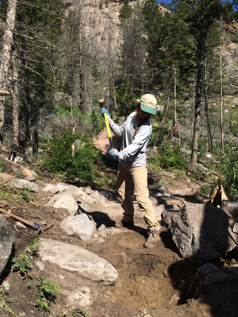 A woman working on a trail in the woods.
