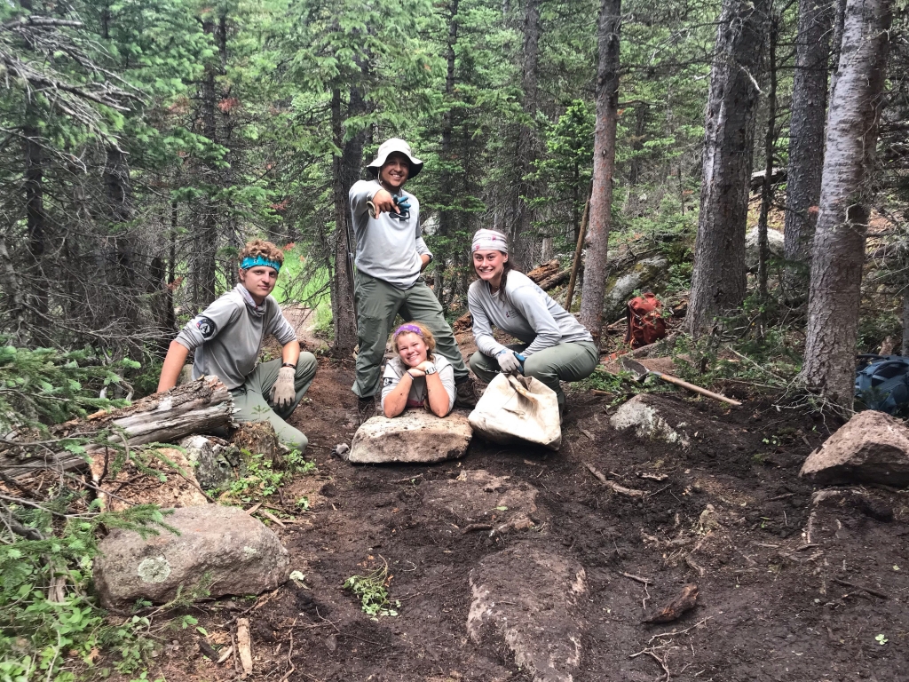 Four people posing on a trail in the woods.