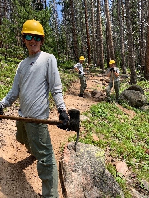 A group of hikers carrying an ax on a trail.