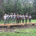 A group of people standing on a wooden bridge in the woods.