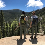 Two hikers standing on top of a rock with their backpacks.