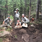 Four people posing on a trail in the woods.