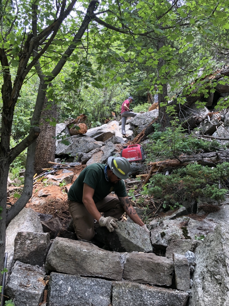 A man working on a rock wall in the woods.