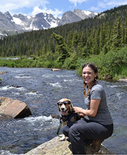A woman with a dog on a rock next to a river.