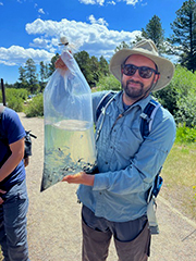 Two men standing on a trail holding a bag of water.