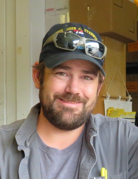 A man wearing a hat and sunglasses is smiling.