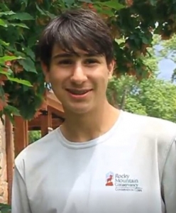A young man smiling in front of a tree.