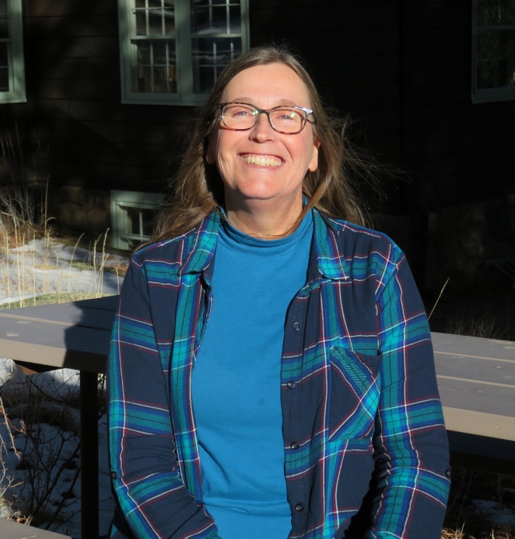 A woman wearing glasses and a plaid shirt sitting on a bench.