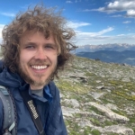 A man with curly hair standing on top of a mountain.