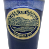 Blue shot glass featuring an embossed emblem of Rocky Mountain National Park with a mountain and forest scene, inscribed "Established 1915.