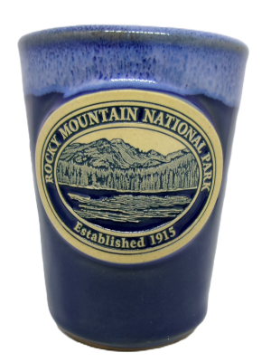 Blue shot glass featuring an embossed emblem of Rocky Mountain National Park with a mountain and forest scene, inscribed "Established 1915.