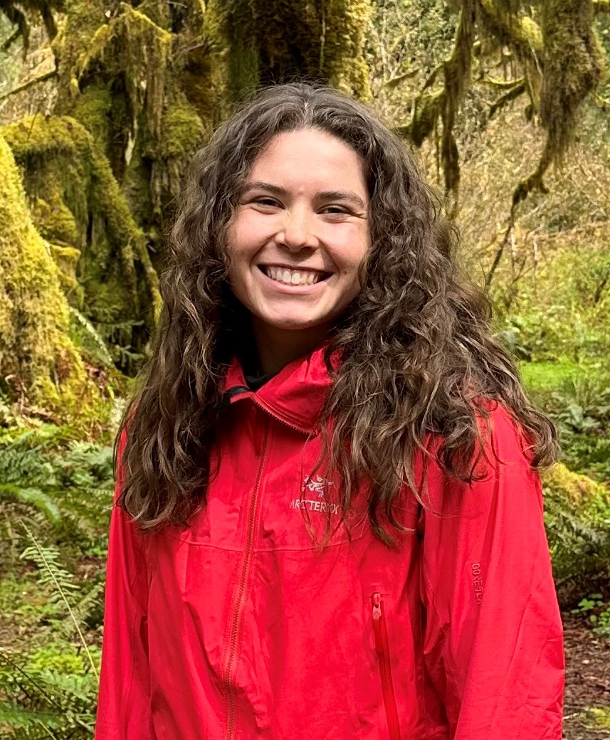 A young woman in a red jacket standing in a forest.