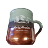 Copper mug A green and brown mug with the Rocky Mountain National Park emblem, showcasing a design of mountains, trees, and a moose, known as the RMNP Copper Bottom Mug.
