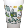 A pint glass featuring colorful graphic illustrations of trees, animals, and nature scenes, with "RMNP" and partially visible “NATIONAL PARK” text. Product name: Glass - RMNP Pint Mod Collage.