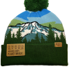 The Snowy Mountains Beanie is a green hat featuring a mountain and forest design with a pom-pom, plus labels reading "HEADS COZY, PLANET BREEZY." and "NORTHERN." on a brown patch.