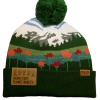 wildflower mtns back The Wildflower Mountains Beanie features green and white knit, a mountain and forest design with red flowers, a large green pom-pom, and labels reading "HEADS COZY. PLANET BREEZY." and "NORTHERN.