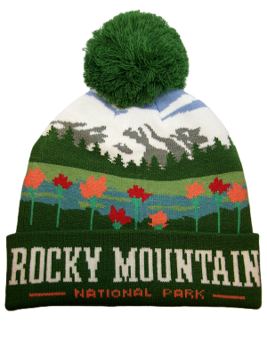 The Hat - Wildflower Mountains Beanie is a green, white, and multicolored beanie with a pom-pom, mountain and tree patterns, and "ROCKY MOUNTAIN NATIONAL PARK" text on the brim.